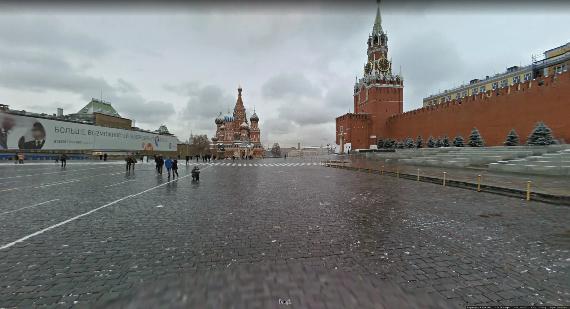 Picture of a flat plaza with Cyrillic posters on the left side. There is a Russian-style Orthodox church in the background