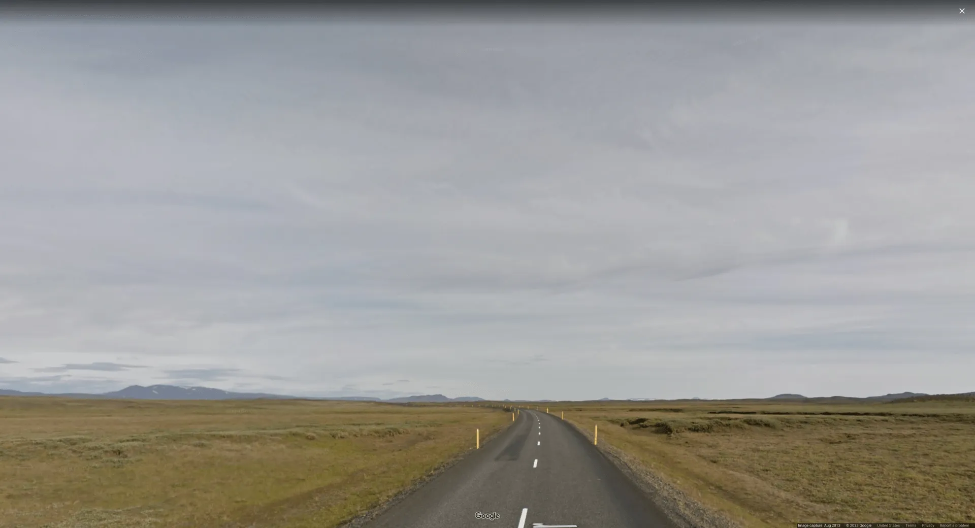 Picture of a road in an extremely flat & empty plains, with overcast skies and yellow reflector poles